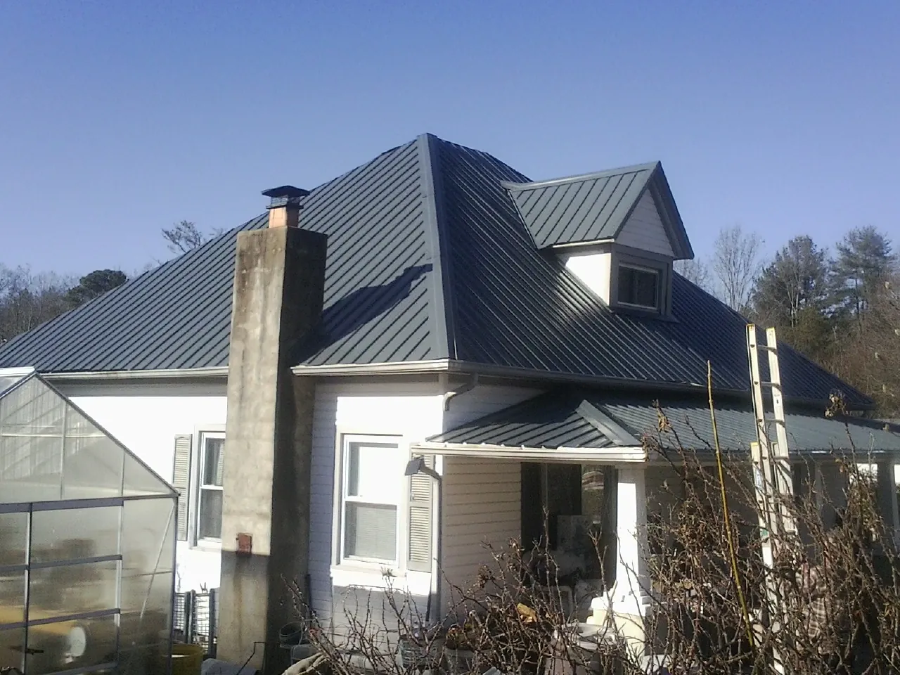 Dark blue standing seam metal roof on a white farmhouse with dormer — Slate & Tile Roof Repair by Roofing Brothers in New Freeport