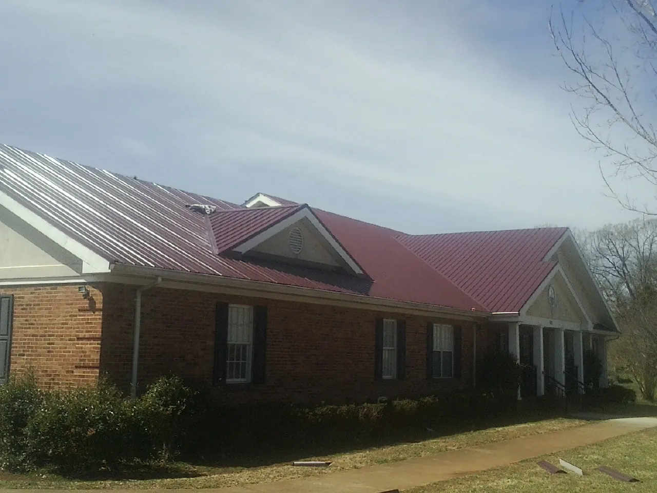 Red metal roof with gabled entries on a long brick building, from a Hail Damage Roof Repair job in New Freeport