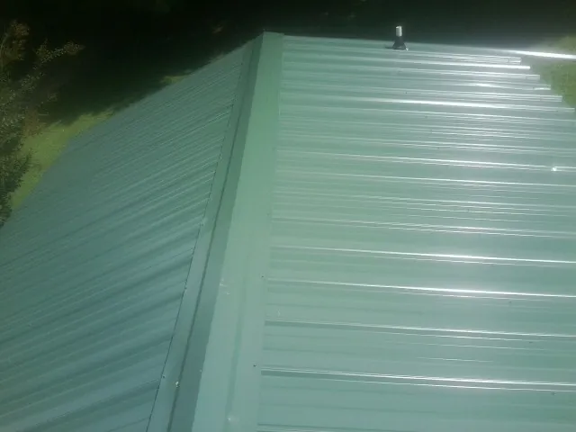 New green metal panels meeting at the ridge of a roof — Flat Roof Repair work by our crew in New Freeport