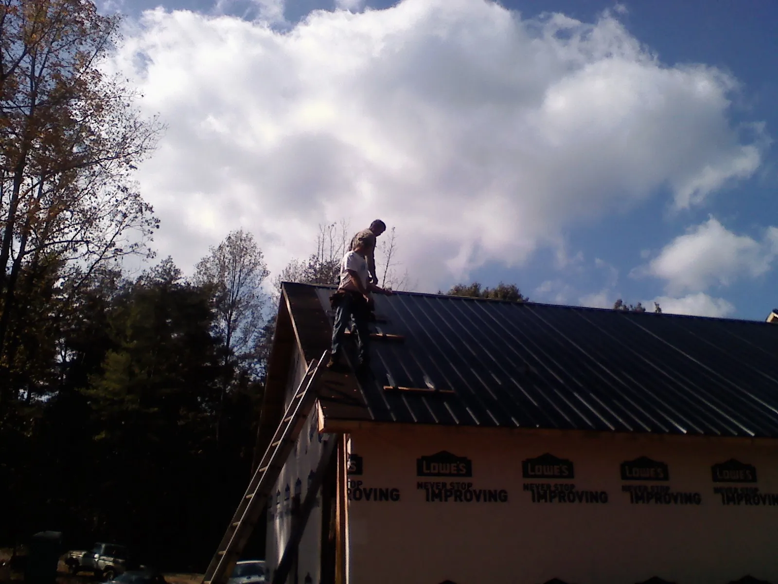 Roofer fastening dark metal panels high against a cloudy sky, from a Roof Inspection job in New Freeport