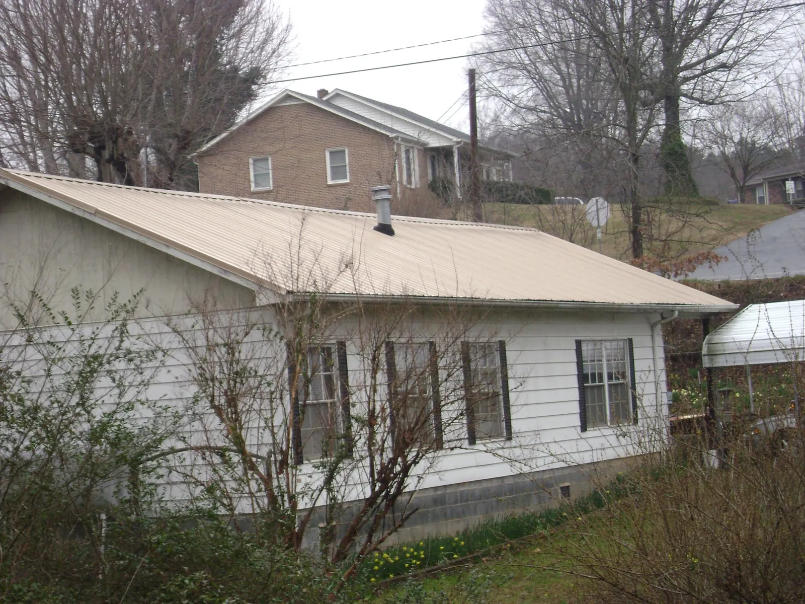 Tan metal roof on a white sided house set into a hillside — Commercial Roofing by Roofing Brothers in New Freeport