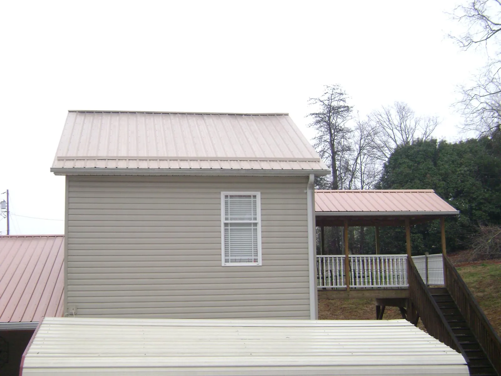 Tan metal roofs on a two story addition and attached porch, from a Roof Replacement job in New Freeport